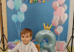 Jasiek siedzi przy urodzinowym stole i pozuje do urodzinowego zdjęcia.
