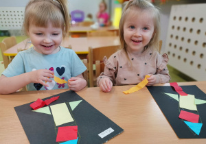 Maja i Julia przyklejają figury tworząc obrazek rakiety.