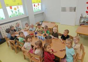 Dzieci siedzą przy stole i czekają na zrobienie koktajlu truskawkowego.