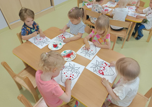 Dzieci przy użyciu czerwonej farby odznaczają paluszkami kolorowankę truskawkę.