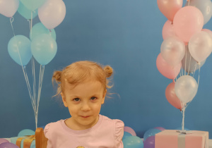 Marysia siedzi przy stoliku i pozuje do zdjęcia, czekając na poczęstunek.