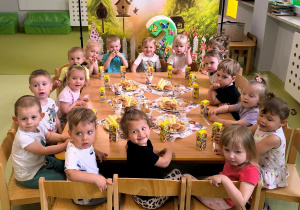 Dzieci siedzą przy stoliku i jedzą urodzinowe smakołyki.
