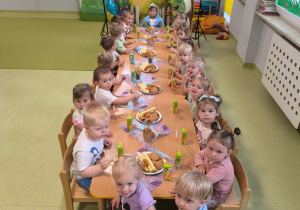 Dzieci siedzą przy stole i jedzą urodzinowe smakołyki.