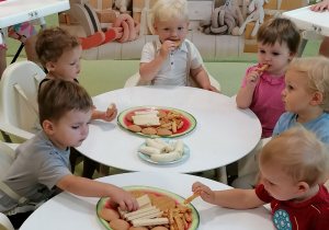 Nicolas z dziećmi siedzi przy stoliku i je ciastko.