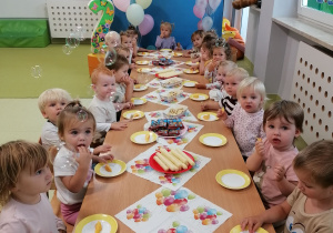 Dzieci siedzą przy stoliku i jedzą słodki poczęstunek.