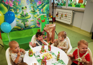 Antoś z dziećmi siedzą przy urodzinowym stole i jedzą smakołyki.
