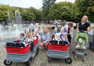 Dzieci i opiekunki na spacerze z wózkami.