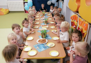 Dzieci siedzą przy stoliku i jedzą poczęstunek z okazji Dnia Chłopca.