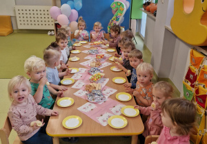 Dzieci siedzą przy stole i jedzą słodki poczęstunek.