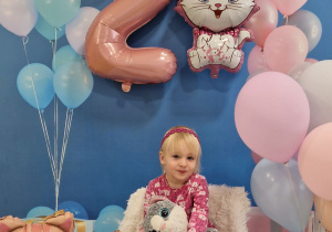 Ania z pluszowym kotkiem pozuje na urodzinowym tle.