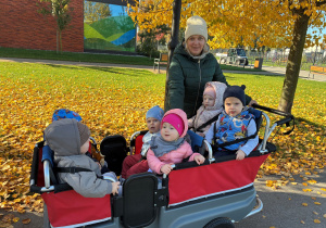 Dzieci siedzą w wózku spacerowym i obserwują otaczającą je przyrodę.