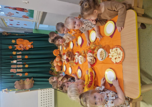 Dzieci siedzą przy stole i jedzą słodki poczęstunek.