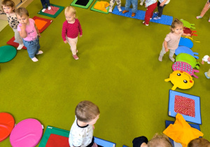 Na dywanie rozłożona jest ścieżka sensoryczna. Dzieci przechodzą po niej jeden za drugim.