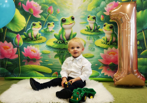 Leon siedzi na dywanie, pozuje do urodzinowego zdjęcia.