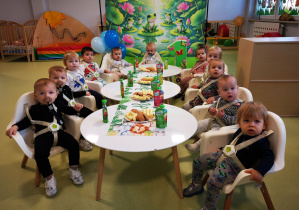 Dzieci siedzą przy stolikach i jedzą urodzinowy poczęstunek.