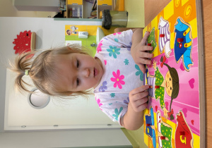 Marcelina siedzi przy stoliku i układa drewniane puzzle.