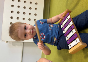 Mark siedzi na dywanie i gra na cymbałkach.