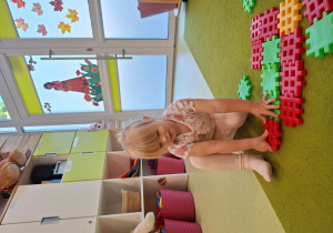 Gabrysia układa klocki na dywanie.