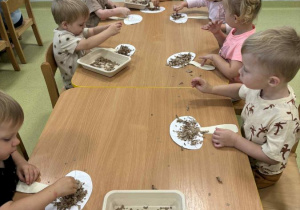 Dzieci posypują papierowego grzyba brązową bibułą.