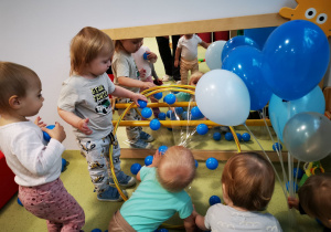 Dzieci przyklejają niebieskie piłeczki do koła pokrytego taśmą klejącą.