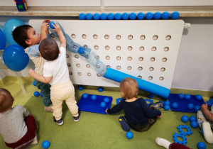 Dzieci bawią się piłkami wrzucając je do toru utworzonego z butelek i kartonu.