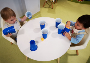 Kobi i Mateusz bawią się piłeczkami przekładając z kubeczka do kubeczka.