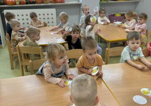 Dzieci siedzą przy stolikach i oglądają obrazki z warzywami i owocami.