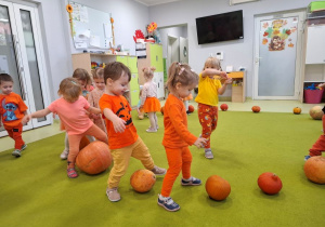 Dzieci wykonują na dywanie slalom wokół dyni.
