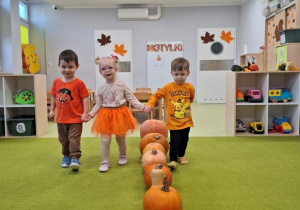 Laura, Leon i Kuba spacerują na dywanie oglądając dynie.