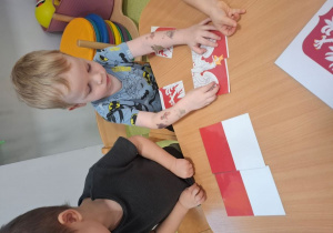 Mikołaj układa przy stoliku puzzle z Godłem Polski.