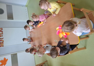 Dzieci siedzą przy stoliku i dmuchają wiatraki.