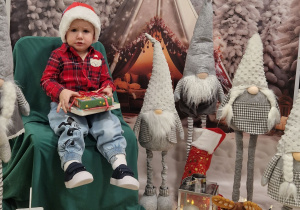 Ivo z prezentem siedzi na krześle i pozuje do sesji mikołajkowej.