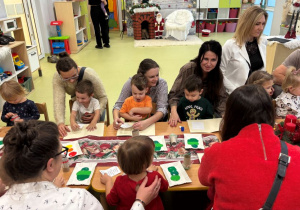 Dzieci wraz z rodzicami wykonują kartkę bożonarodzeniową przy stolikach.