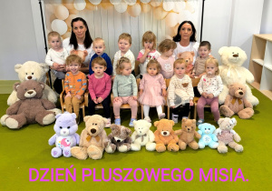 Dzieci siedzą na dywanie z opiekunkami. Przed nimi ustawione są pluszowe misie. Jest to zdjęcie grupowe.