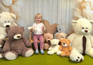 Pola siedzi na krzesełku. Obok stoją misie. Za Polą powieszone jest tło z okazji dnia misia.