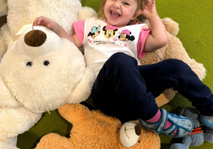 Tosia leży na dywanie. Obok leży dużo pluszowych misiów.