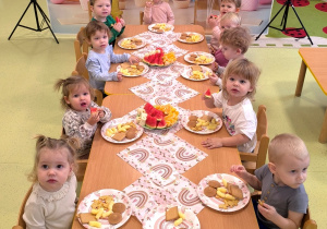 Dzieci siedzą przy stolikach i jedzą słodki poczęstunek przygotowany przez rodziców Apolonii.