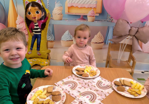 Apolonia i Ignacy siedzą przy stole i jedzą słodki poczęstunek.