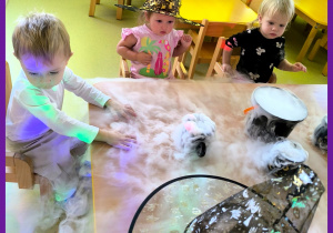 Andrzejki. Dzieci siedzą przy stoliku i oglądają doświadczenie z wykorzystaniem suchego lodu.