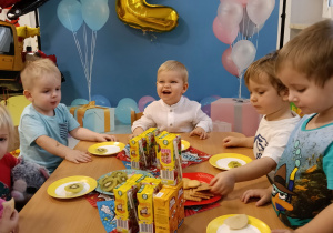 Kuba siedzi przy stoliku i częstuje się urodzinowymi przekąskami.
