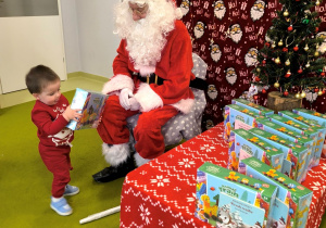 Św. Mikołaj siedzi na krześle. Dawidek podchodzi do Mikołaja i odbiera swój prezent.