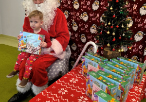 Św. Mikołaj siedzi na krześle. Na kolanach u Mikołaja siedzi Filipek i razem pozują do zdjęcia.