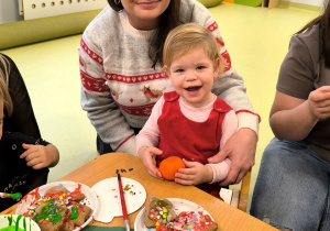 Hania z mamą siedzą przy stoliku. Razem dekorują pierniczki i pozują do zdjęcia.