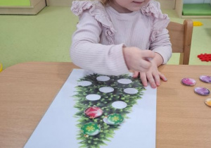 Jagna przykleja bombki na papierową choinkę przy stoliku.