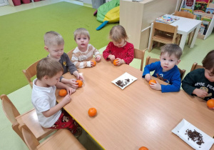 Dzieci wbijają goździki w mandarynki siedząc przy stoliku.