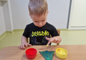 Ivo paluszkami umoczonymi w farbie dekoruje papierową choinkę.