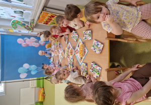 Dzieci siedzą przy stole i częstują się urodzinowymi przekąskami.