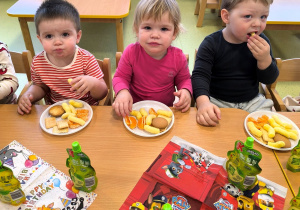 Dzieci siedzą przy stole i jedzą urodzinowy poczęstunek.