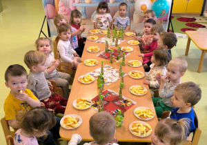 Wszystkie dzieci siedzą przy stole i jedzą urodzinowy poczęstunek.