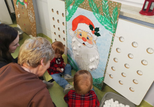 Kuba i Mikołaj bawią się z mamą i ciocią w przyklejanie waty do brody mikołaja.
